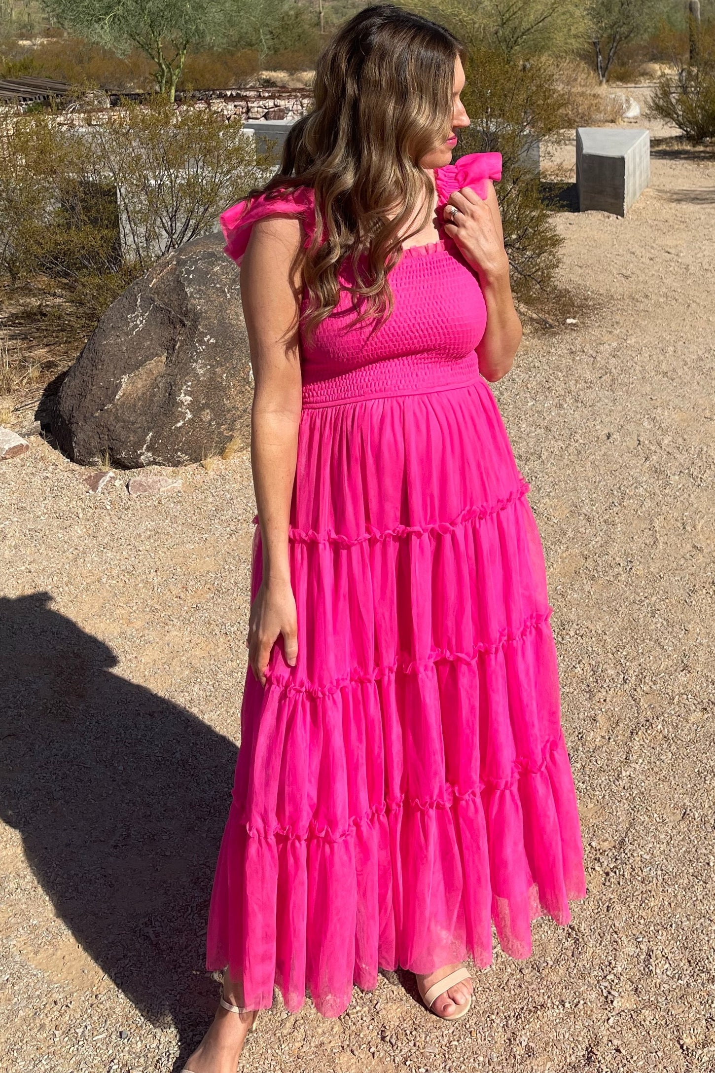woman wearing a fuchsia maxi dress with ruffled straps and tiered layers, standing in a desert landscape