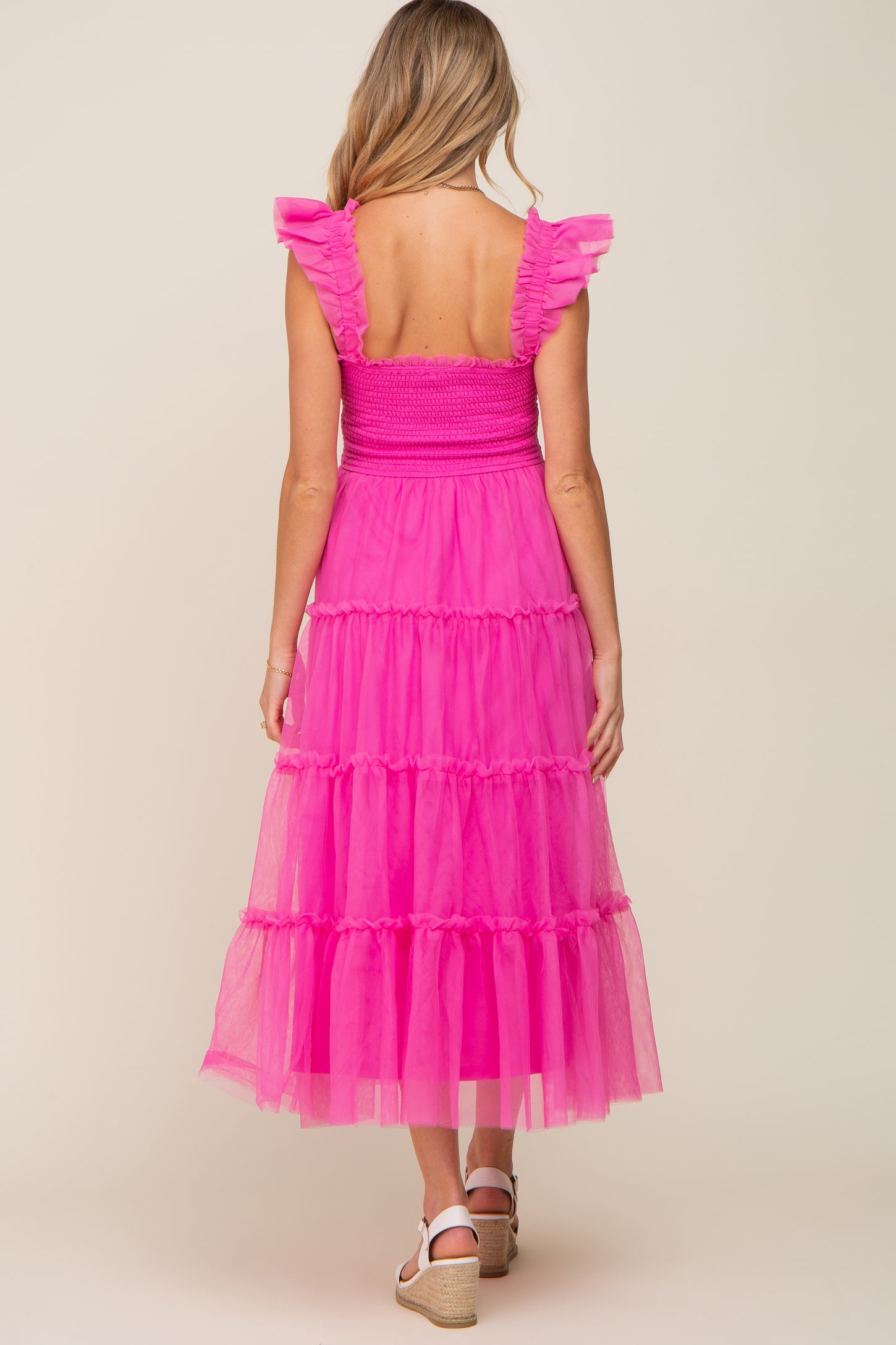 woman wearing a pink tiered maternity dress with ruffled straps, showing a smocked back and ankle length skirt