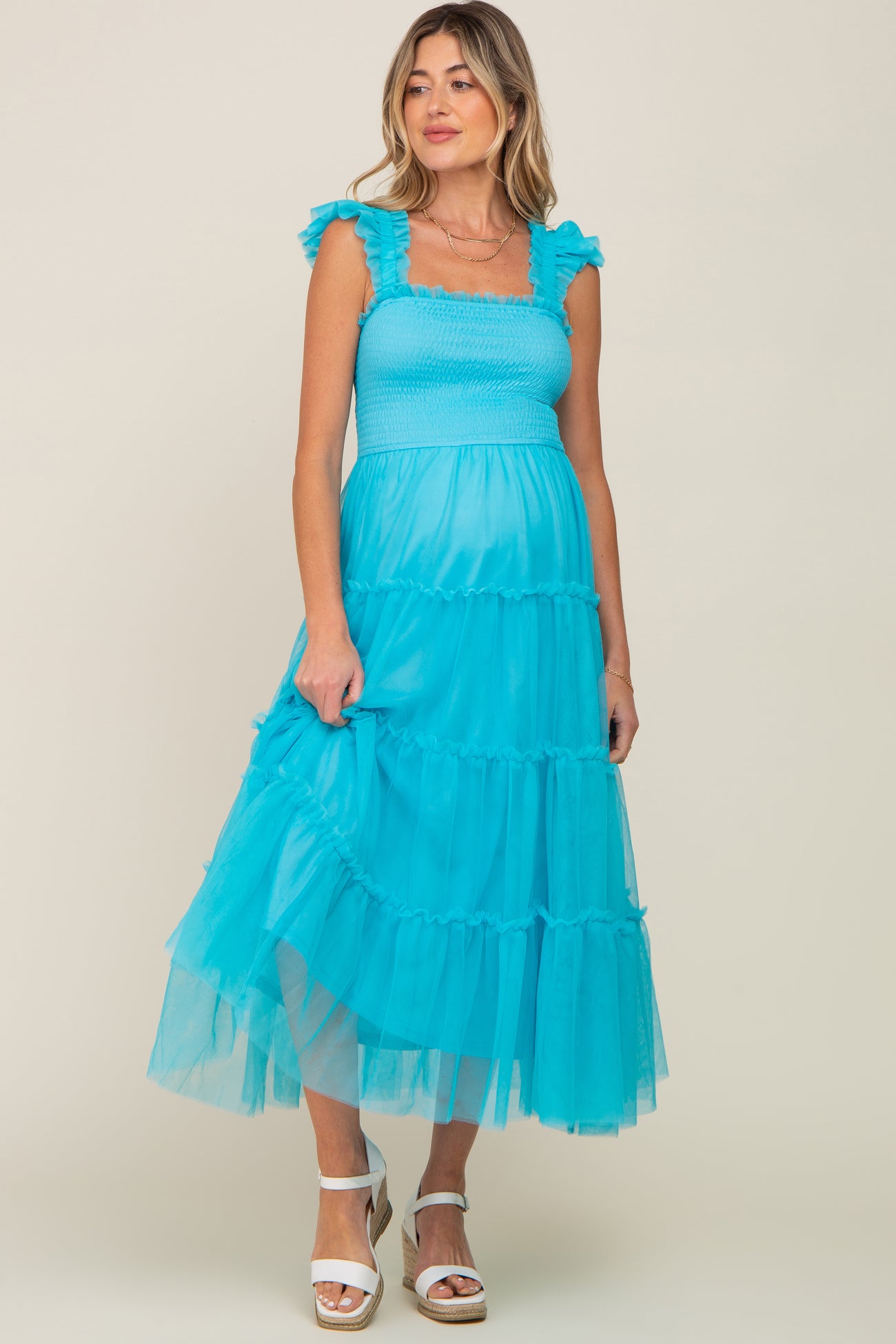 woman wearing a bright turquoise maternity dress with ruffle straps and tiered tulle skirt, showing her baby bump