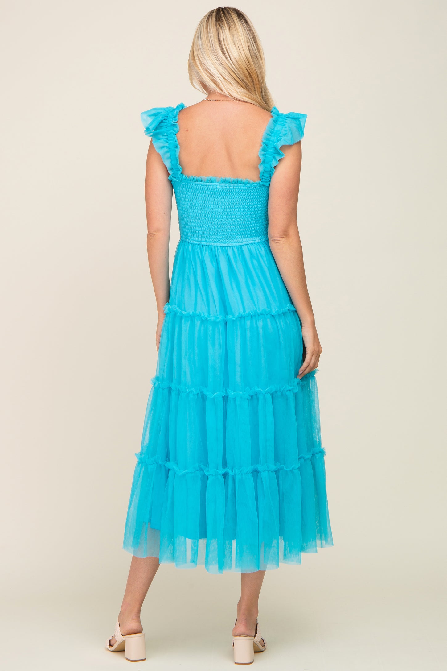 woman wearing a back view of a tiered aqua blue maxi dress with ruffled sleeves and a smocked bodice
