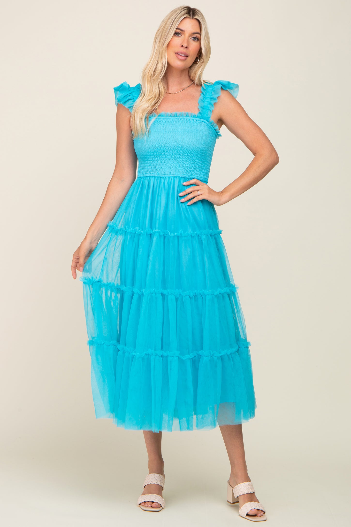 woman wearing a bright turquoise tiered tulle midi dress with ruffle sleeves and a smocked bodice