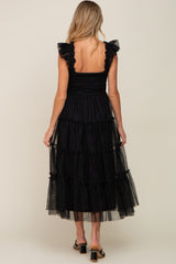 woman wearing a black maternity dress with ruffled sleeves and a tiered tulle skirt, seen from the back