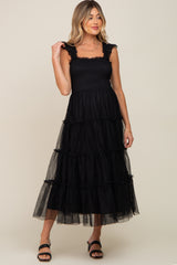 woman wearing a black maternity dress with tiered tulle layers and ruffled straps