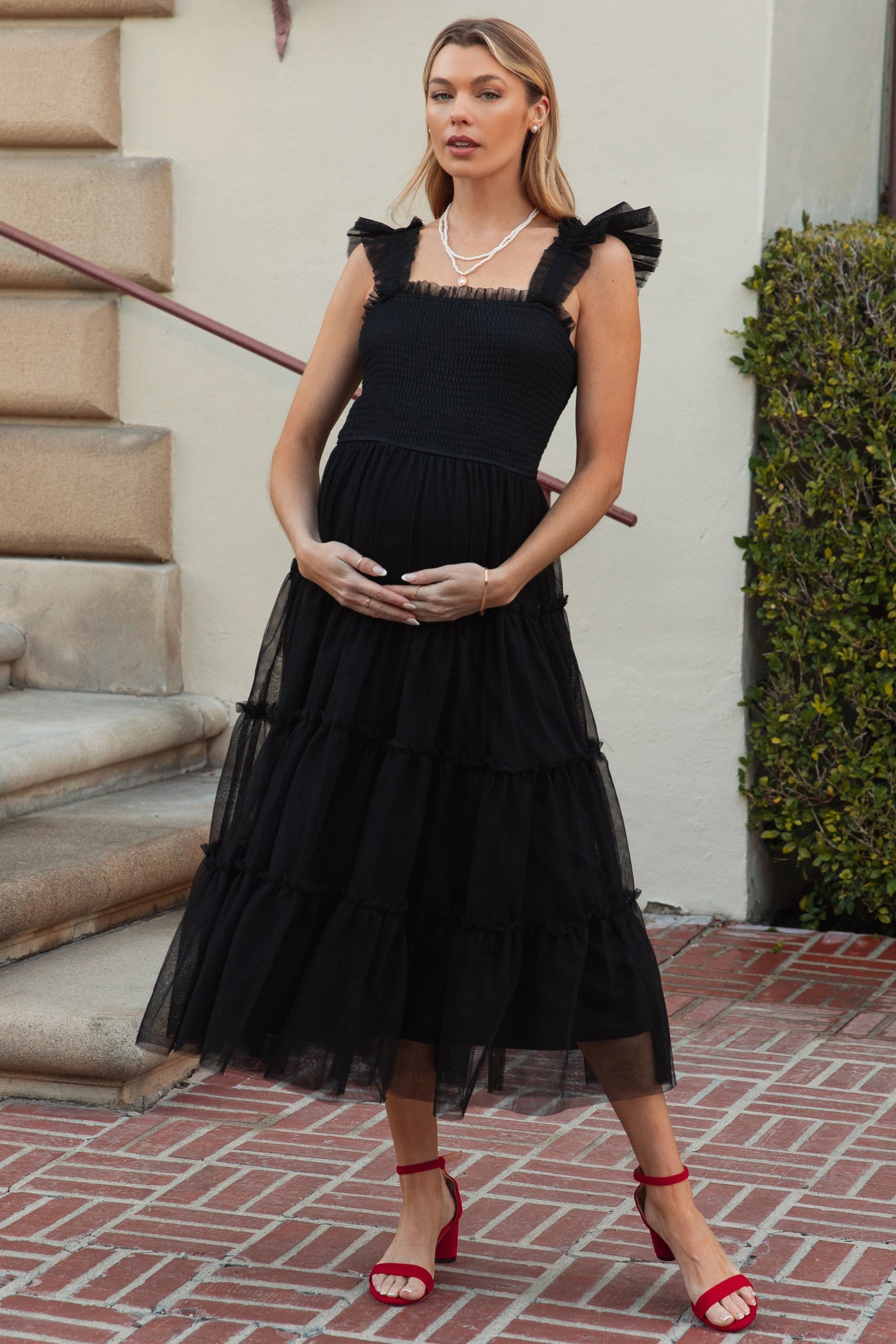 woman wearing a black tiered maternity dress with ruffled straps and holding her baby bump