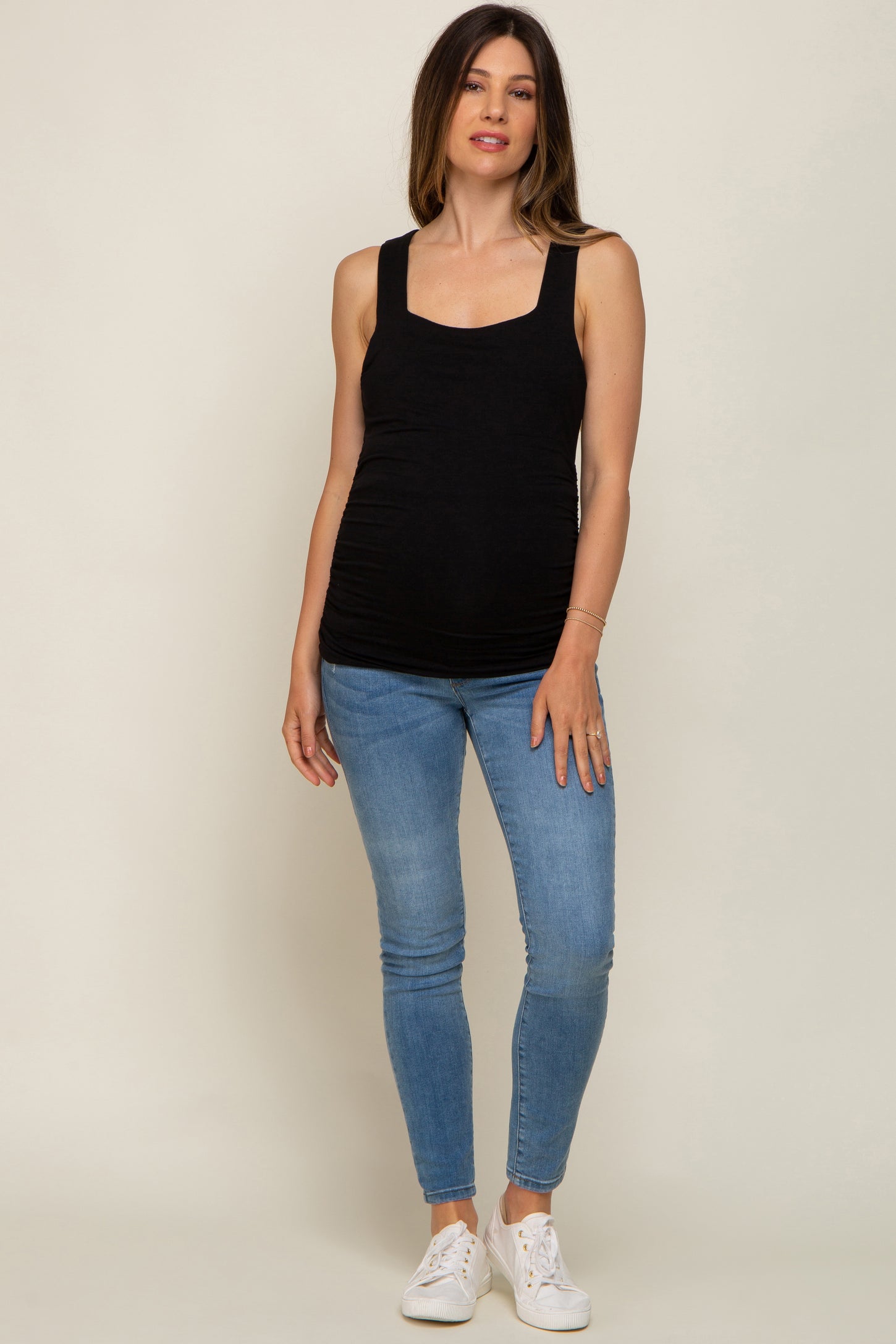 woman wearing a black maternity tank top and blue skinny jeans, showcasing a visible baby bump