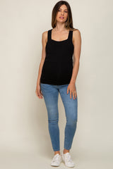 woman wearing a black maternity tank top and blue skinny jeans, showcasing a visible baby bump