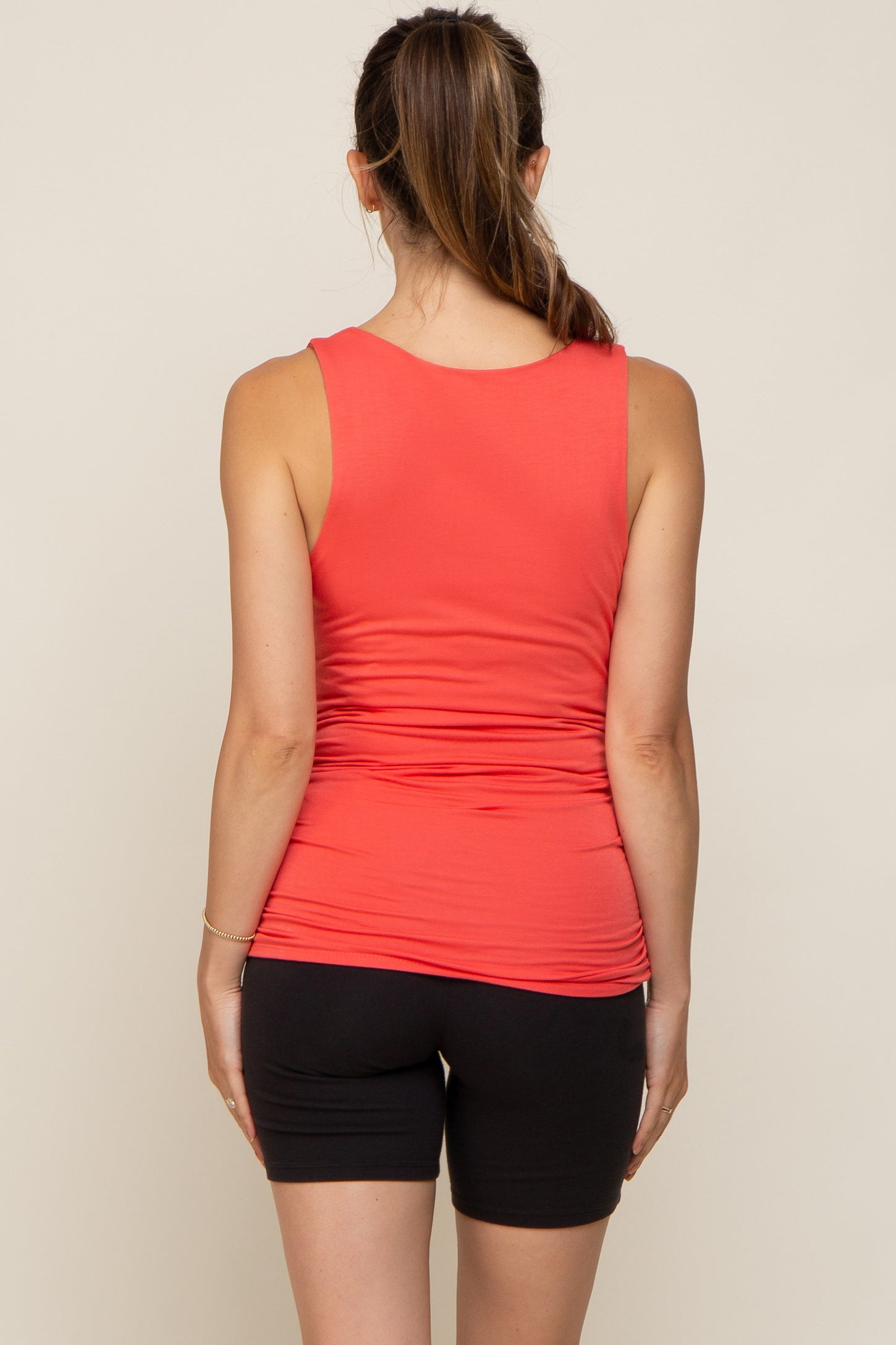 Back view of a woman wearing a coral pink maternity tank top and black biker shorts