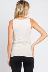Back view of a woman wearing a light beige heathered sleeveless maternity tank top and black leggings
