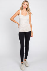 woman wearing a beige ribbed tank top and black leggings with white sneakers against a white background