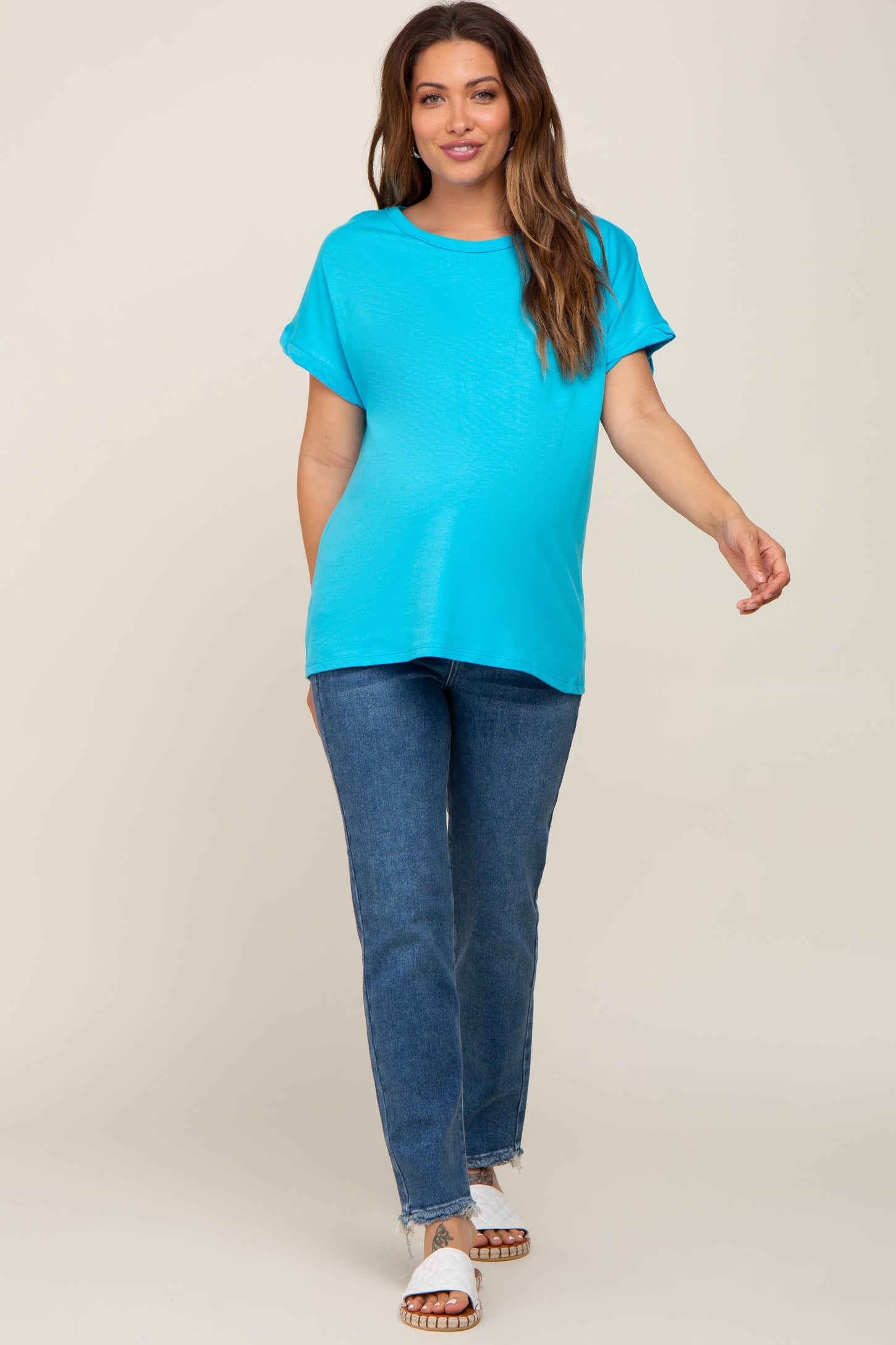 woman wearing a bright blue maternity top with short sleeves and jeans, walking confidently