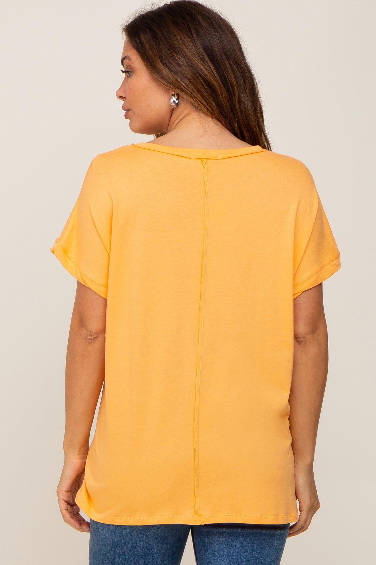 Back view of a woman wearing a yellow short sleeve t-shirt with a vertical center seam and blue jeans