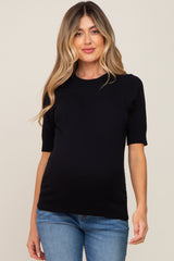 woman wearing a black short sleeve maternity sweater and blue jeans with a visible baby bump