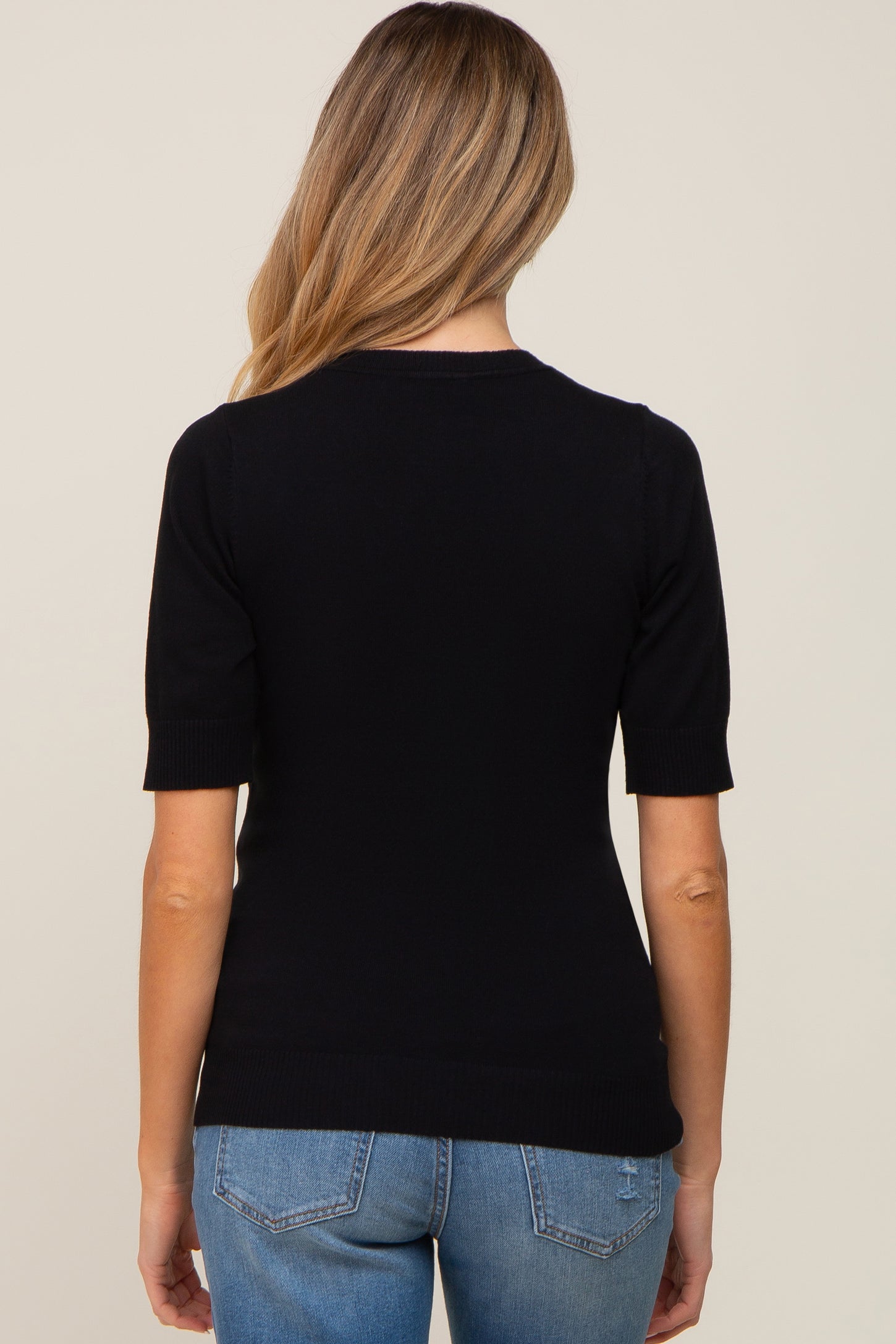 woman wearing a black short sleeve maternity top, view from the back, paired with light blue jeans