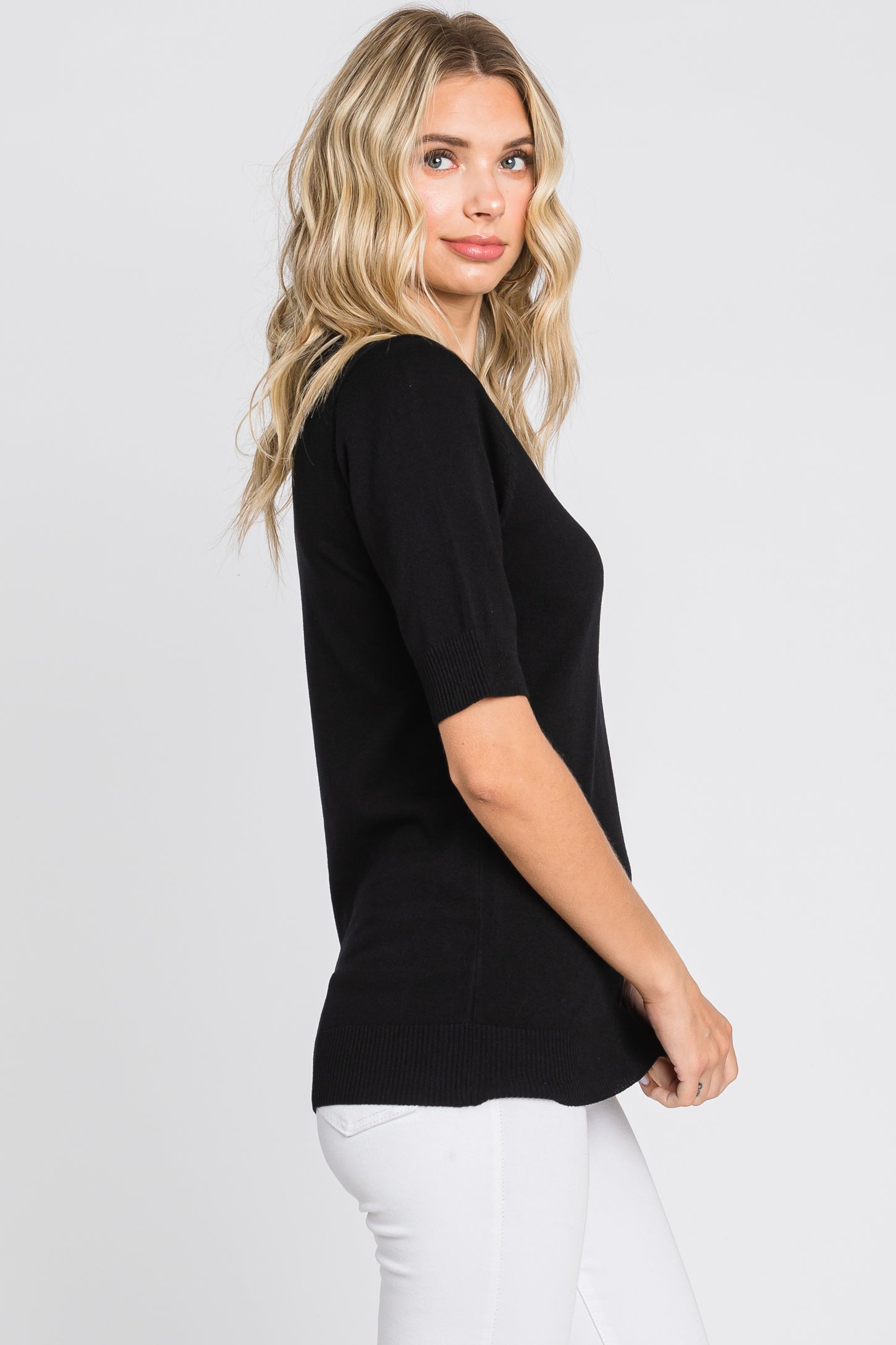 woman wearing a black short sleeve sweater with a relaxed fit and side slits, paired with white jeans