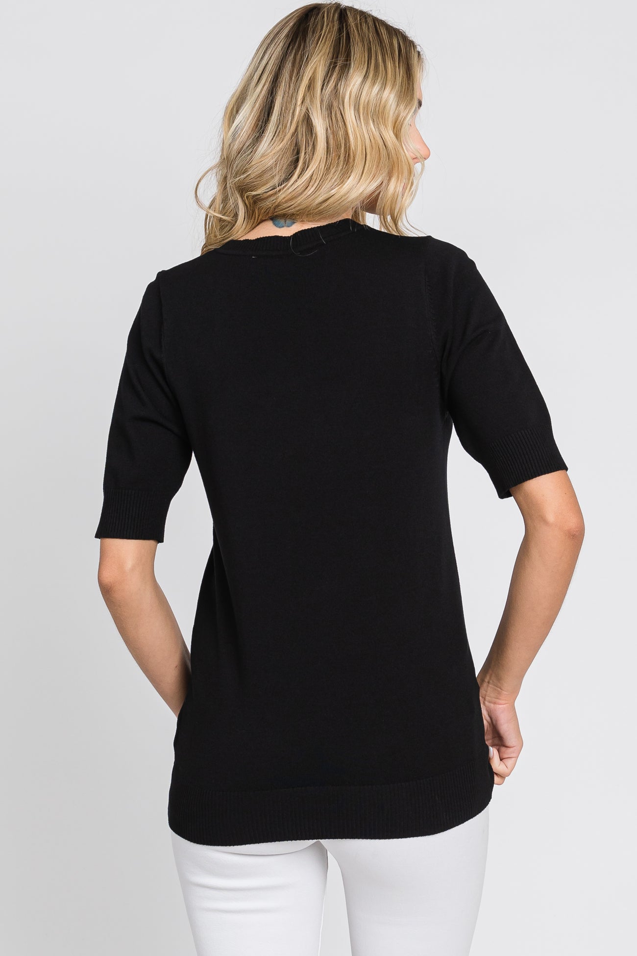 woman wearing a black short sleeve sweater, viewed from the back, paired with white pants