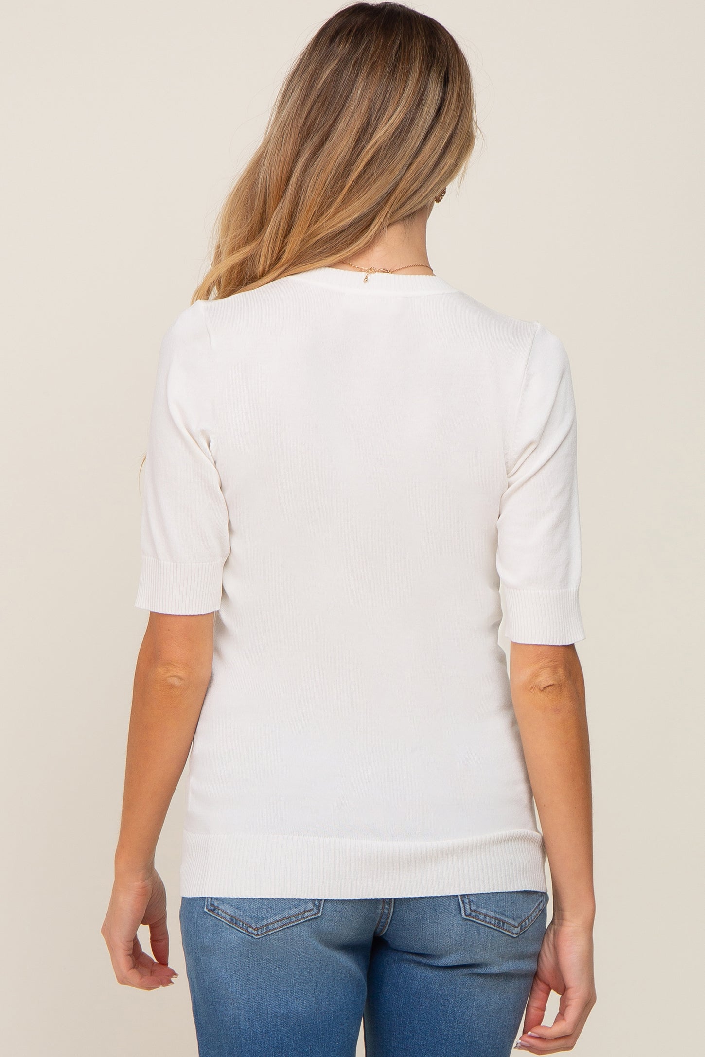 Back view of a woman wearing a white short sleeve knit sweater and blue jeans