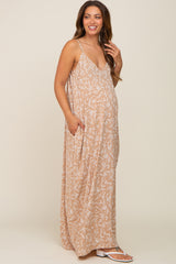 woman wearing a tan leaf print maternity maxi dress with pockets and a visible baby bump