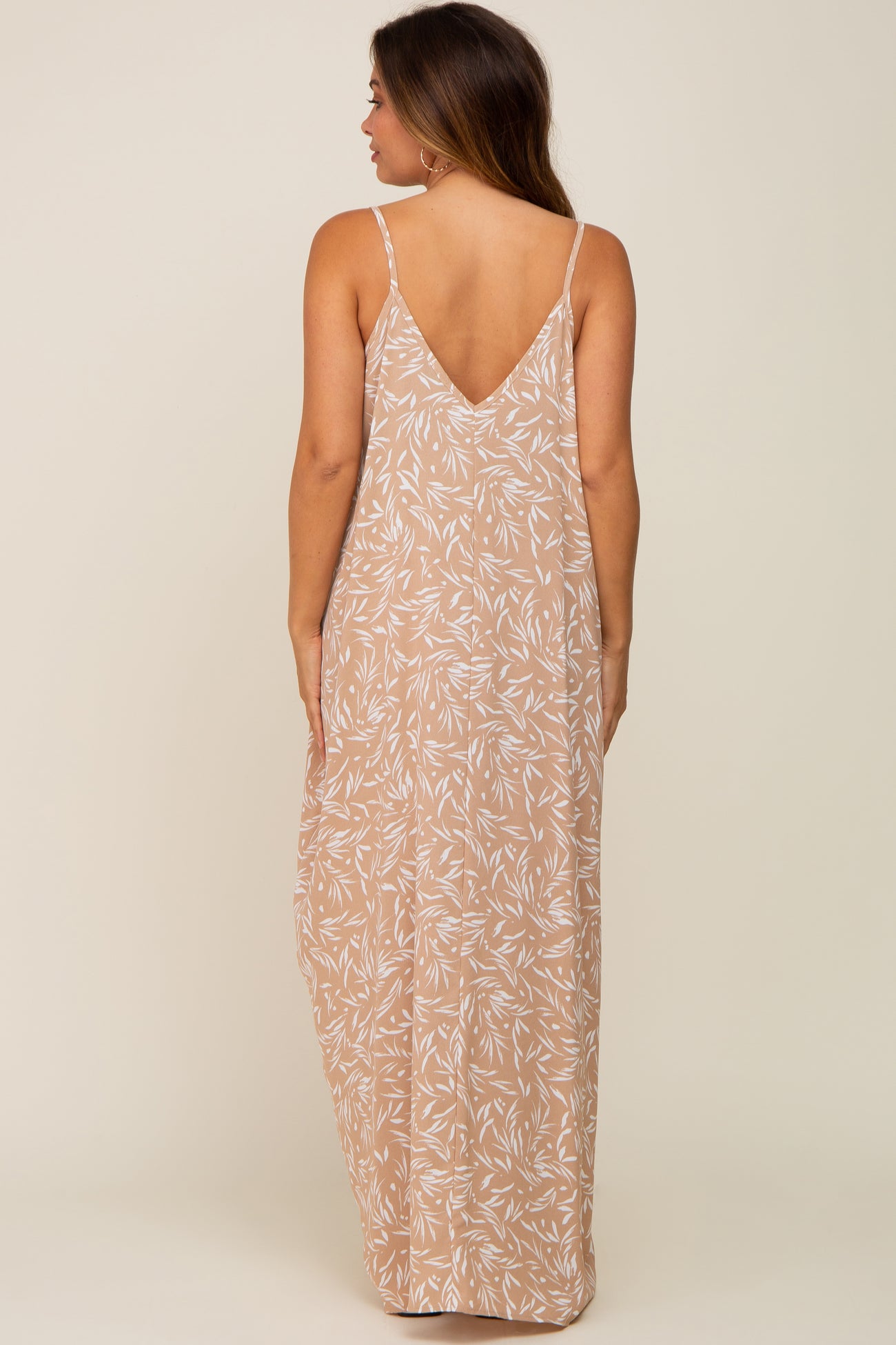 woman wearing a beige maternity maxi dress with white leaf print and thin straps, showing the back view