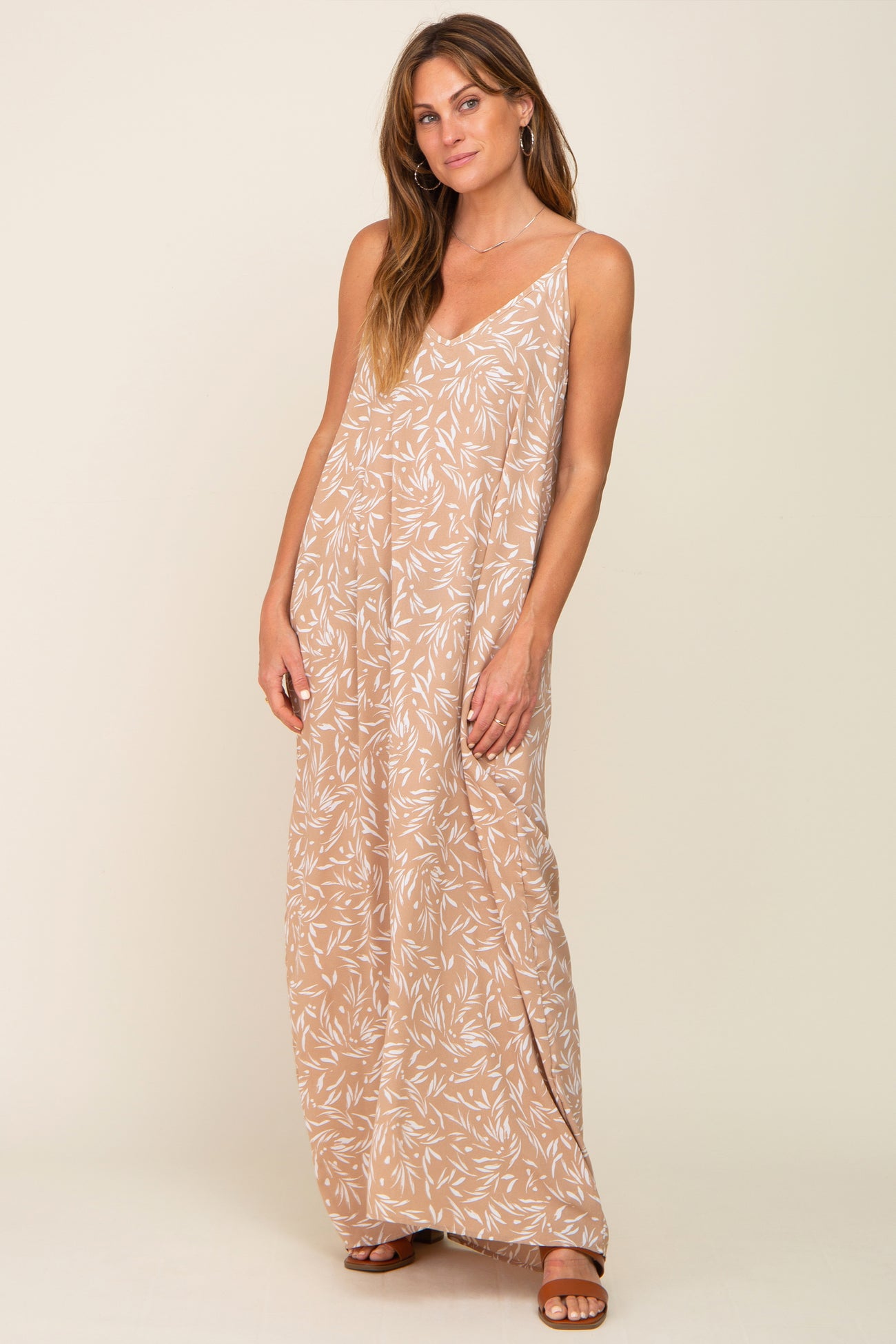 woman wearing a tan leaf patterned maxi dress with a v-neckline and spaghetti straps