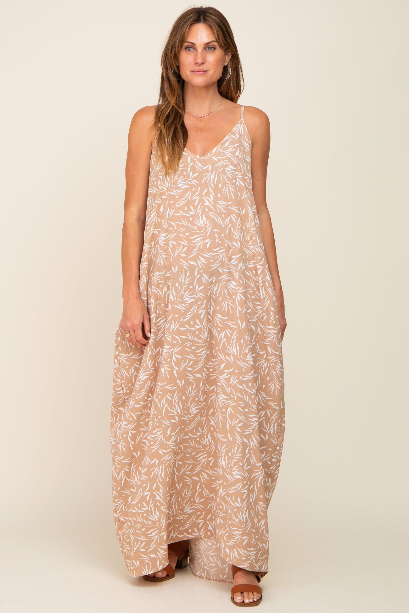 woman wearing a beige maxi dress with a floral pattern and a v-neckline.