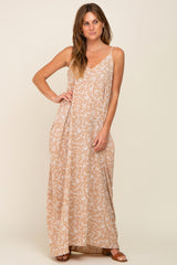 woman wearing a tan maxi dress with a leaf print and thin straps, standing with one hand on her hip