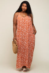 woman wearing an orange floral maxi dress with adjustable straps and side pockets, holding a woven bag