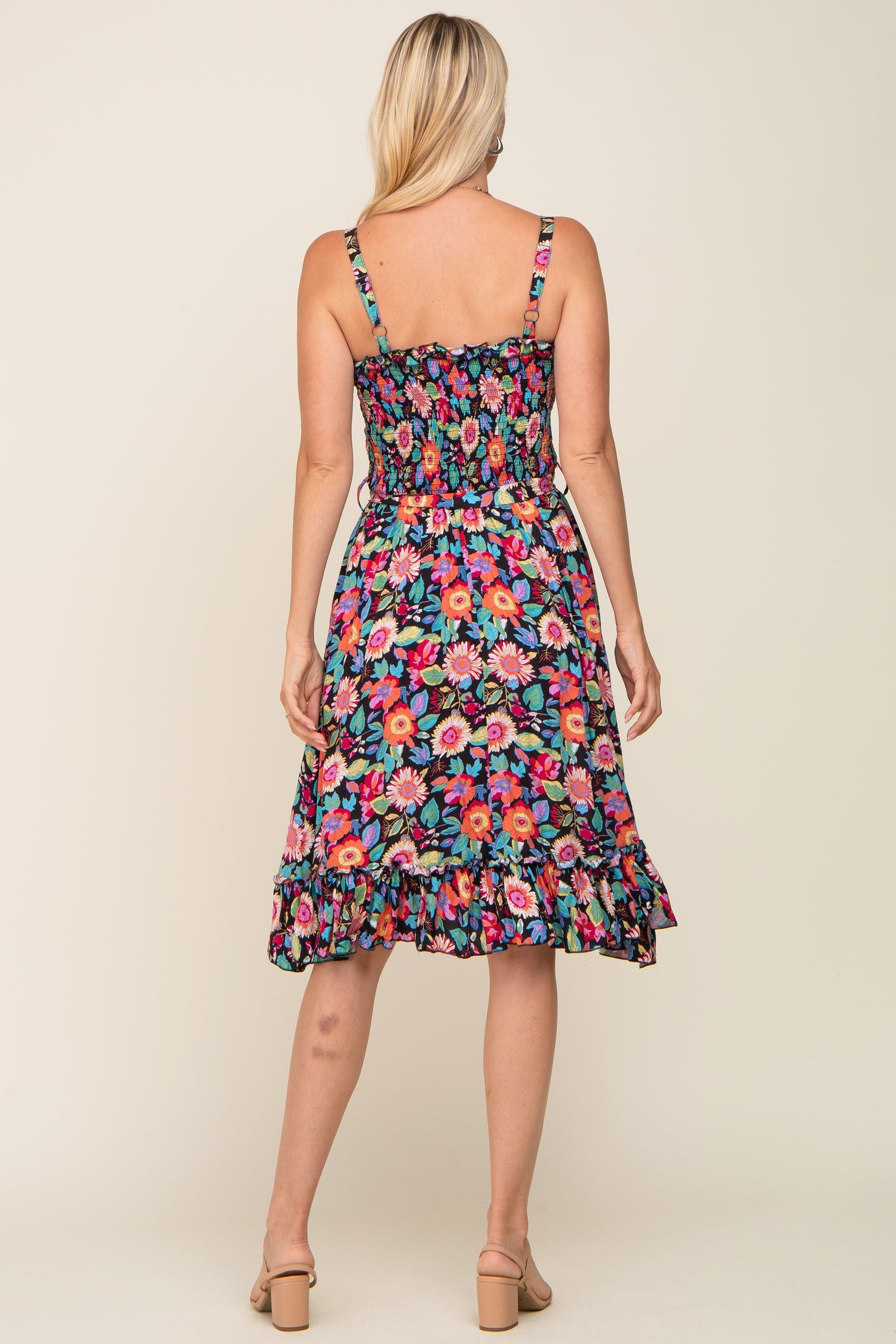 woman wearing a floral print sleeveless dress with a smocked bodice and ruffled hem, seen from the back