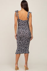 Back view of a woman wearing a black and white floral print maternity midi dress with tie straps and ruched detailing