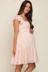 Pregnant woman wearing a light pink smocked maternity dress with ruffle sleeves and lace trim