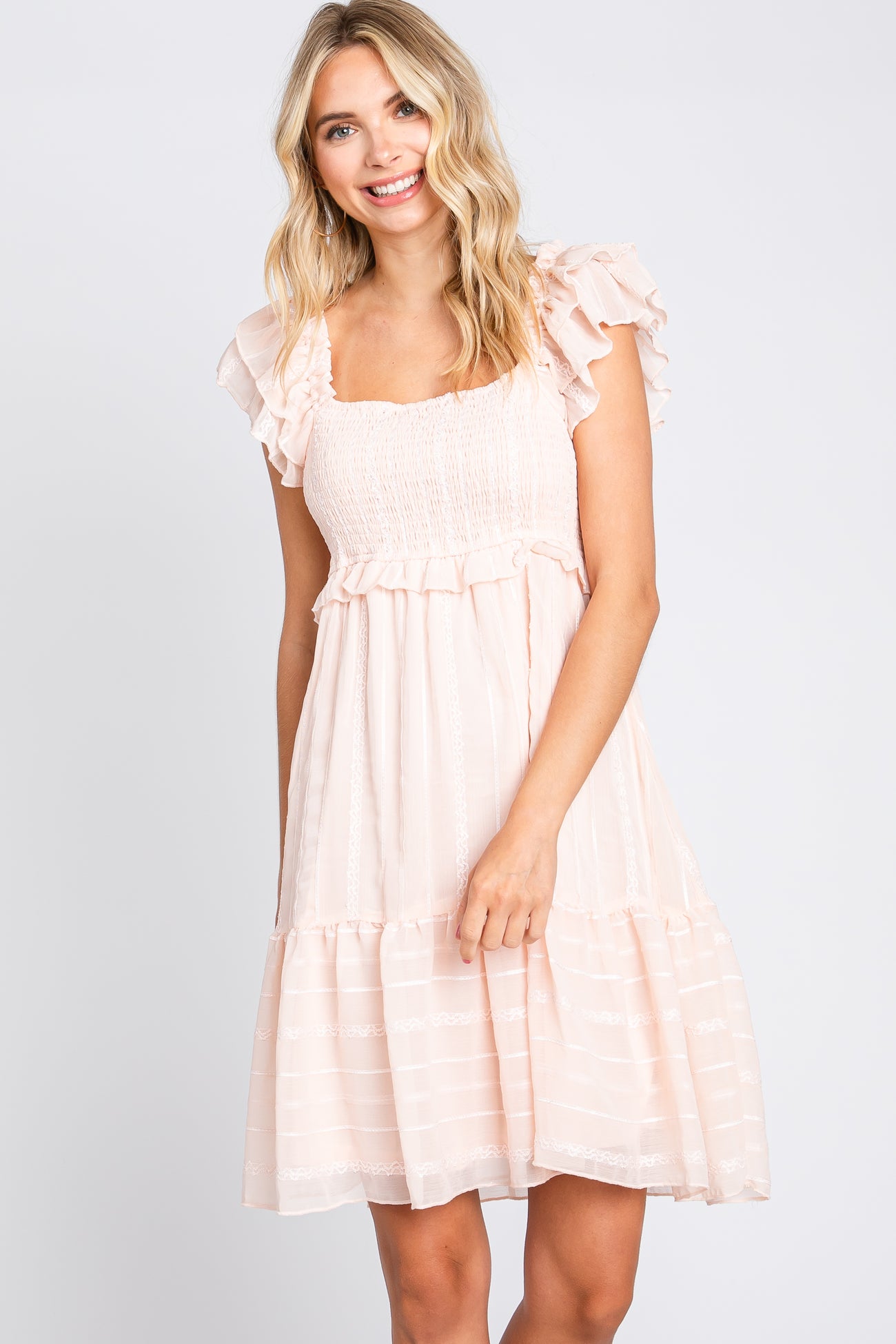 smiling woman wearing a light pink smocked mini dress with ruffle sleeves and tiered skirt