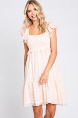 smiling woman wearing a light pink smocked mini dress with ruffle sleeves and tiered skirt
