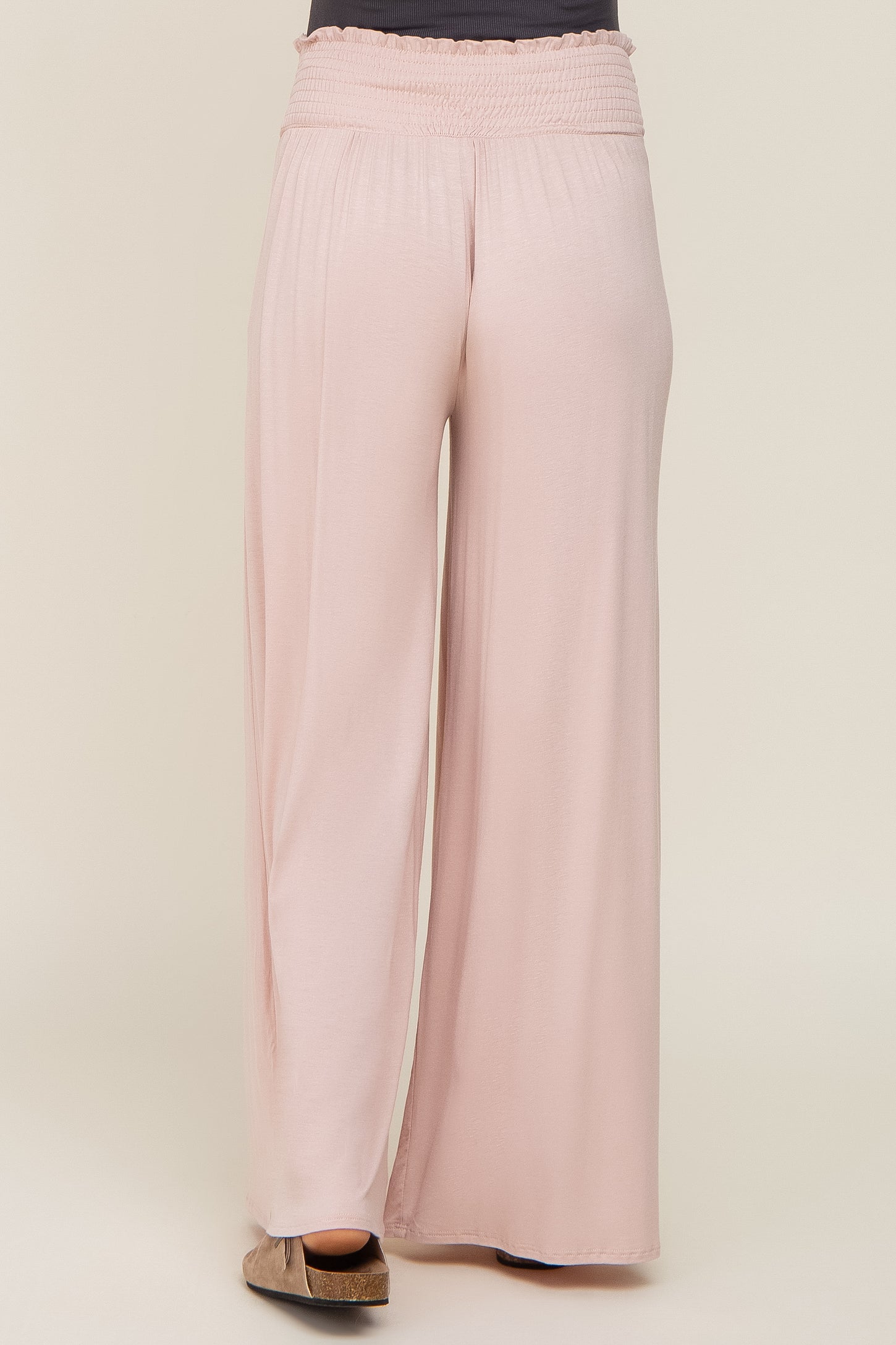 Back view of a person wearing light pink wide-leg pants with a smocked elastic waistband