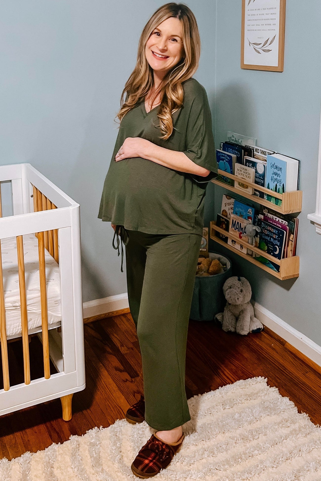 woman wearing a green maternity loungewear set with a tied detail and visible baby bump, standing near a crib