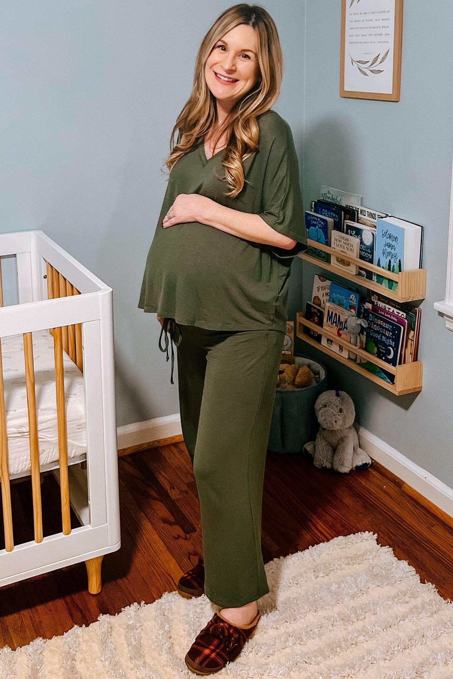 woman wearing a green maternity loungewear set with a tied detail and visible baby bump, standing near a crib