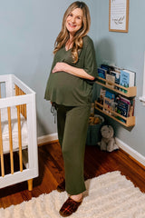 woman wearing a green maternity loungewear set with a tied detail and visible baby bump, standing near a crib