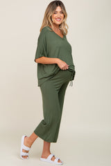 woman wearing a green maternity outfit with a loose top and crop pants, showcasing her baby bump