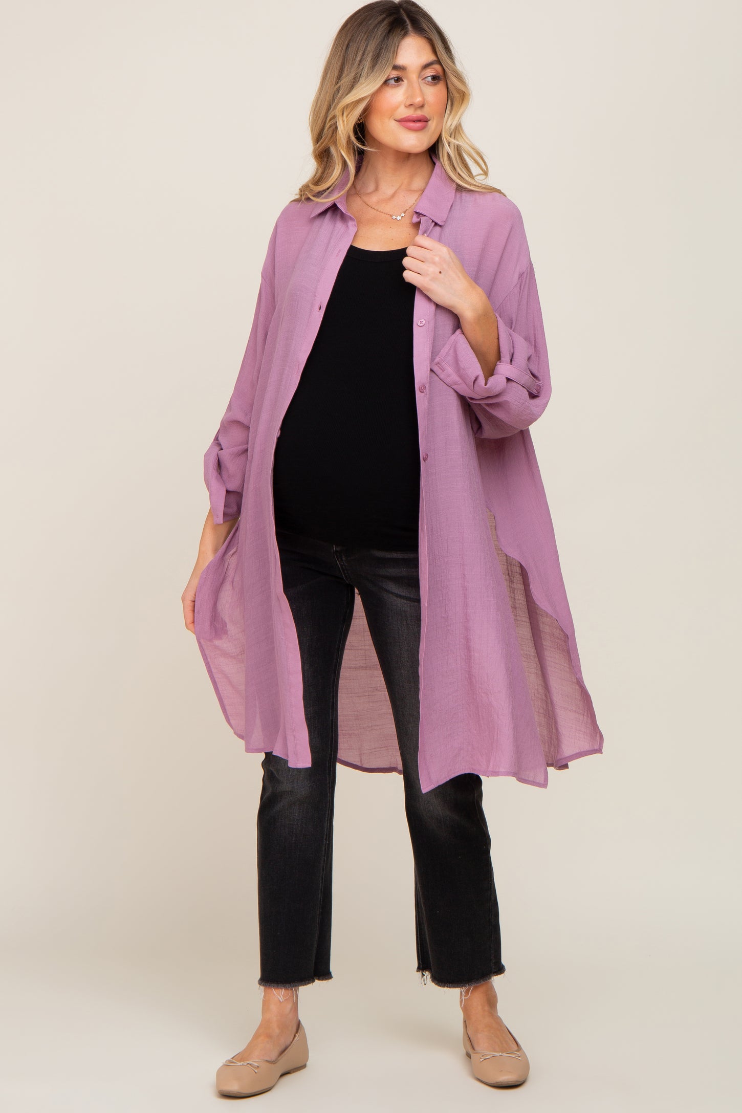 Pregnant woman wearing a long purple button-down maternity shirt over a black top and dark jeans
