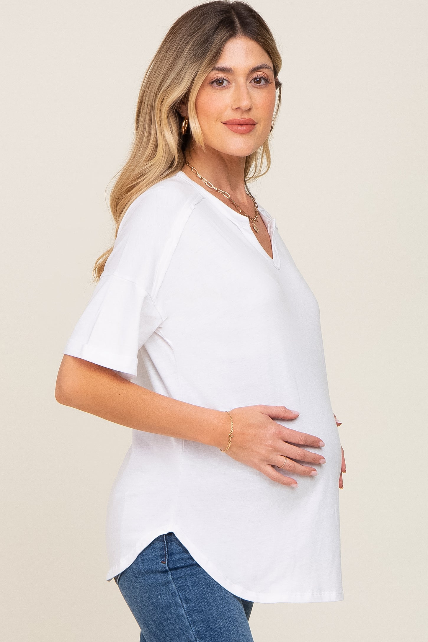 woman wearing a white v-neck maternity top and cradling her baby bump