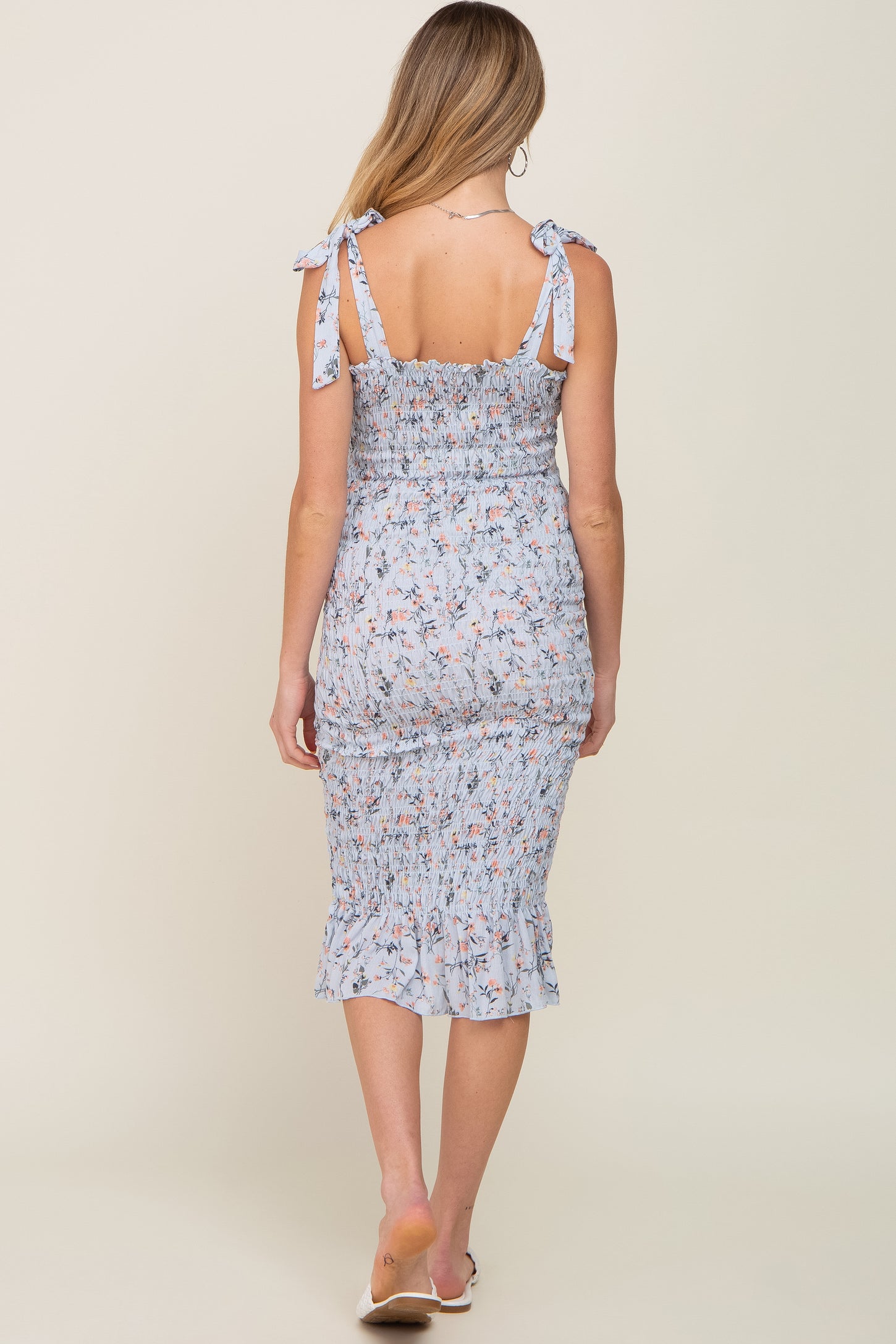 woman wearing a light blue floral maternity dress with tie straps and a smocked design, showing her baby bump