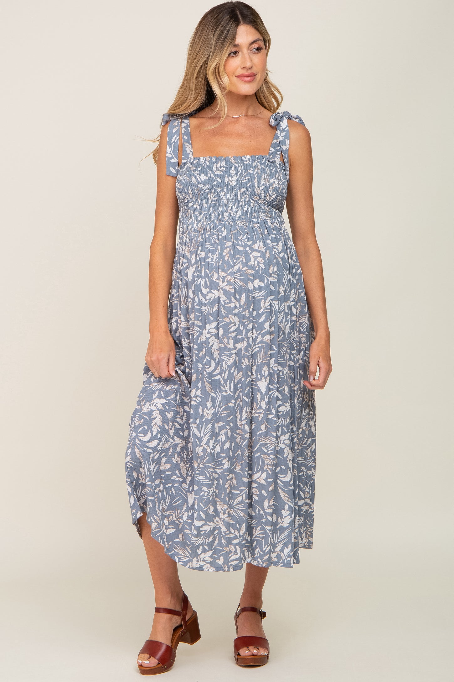woman wearing a blue floral maternity dress with tie straps and a flowing skirt, displaying a baby bump
