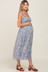 woman wearing a blue floral maternity dress with smocked bodice and holding her baby bump