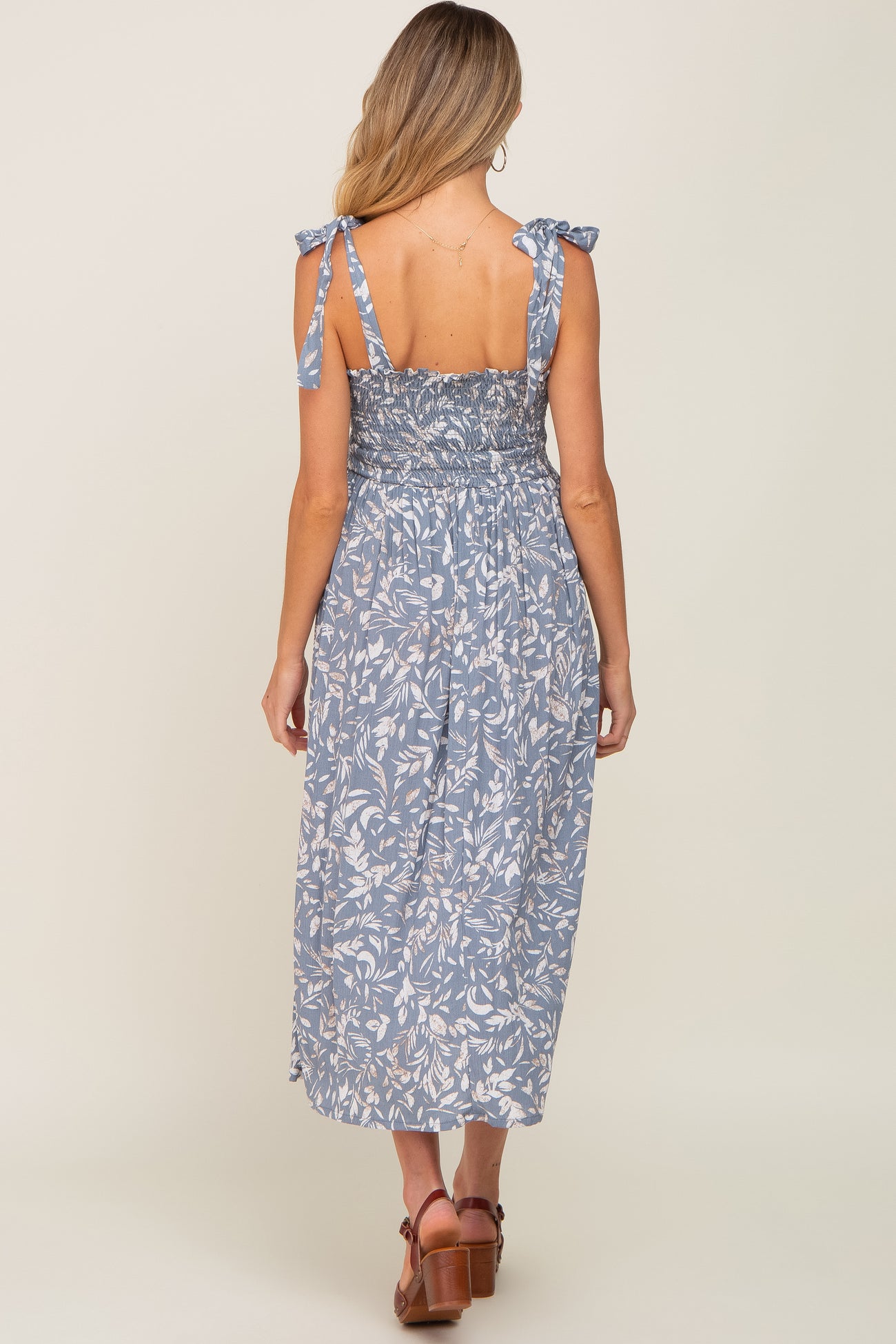woman wearing a blue floral print maternity dress with tie straps, showing the back view and mid-length style