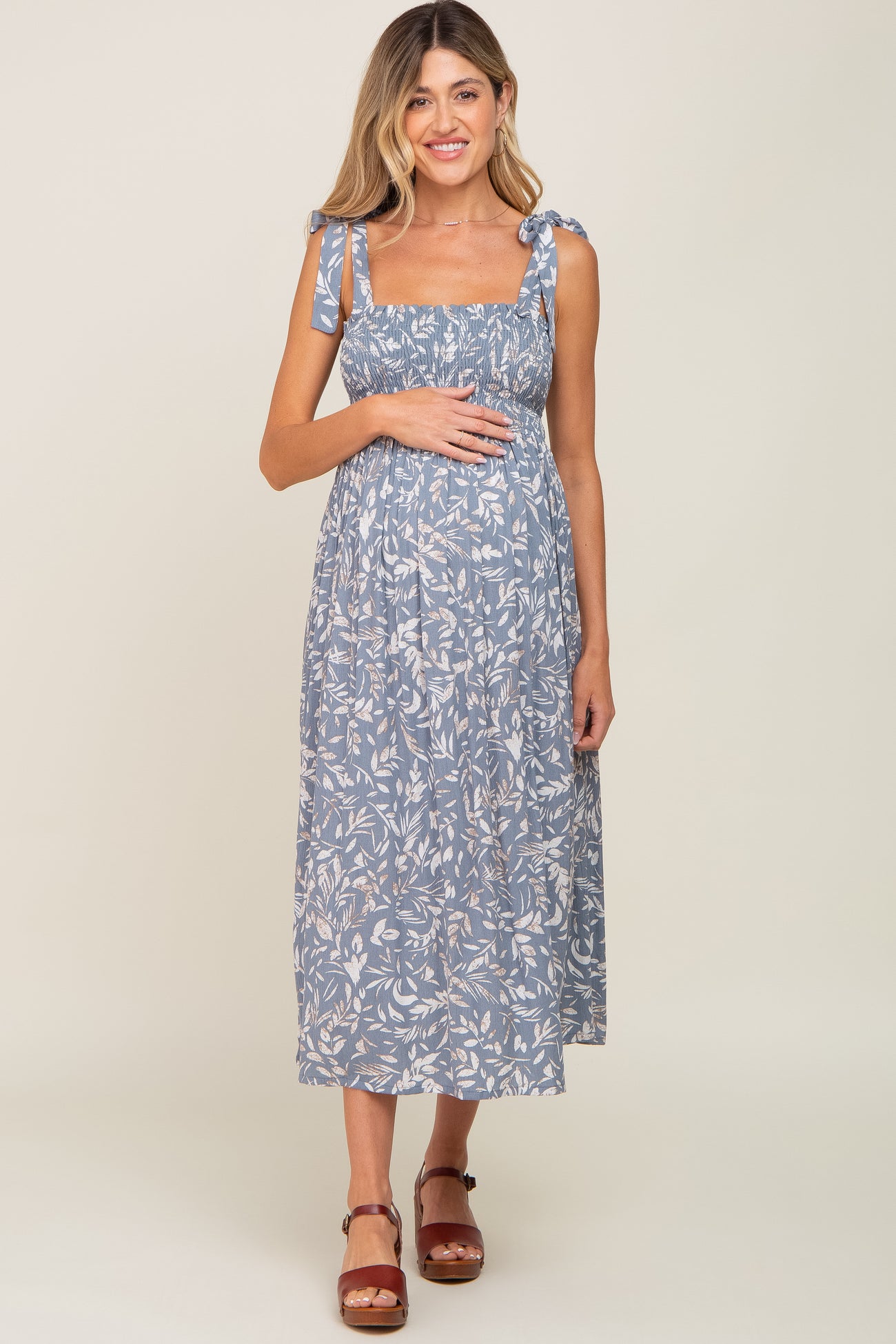 woman wearing a blue floral maternity dress with tie shoulder straps and holding her baby bump