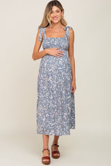 woman wearing a blue floral maternity dress with tie shoulder straps and holding her baby bump