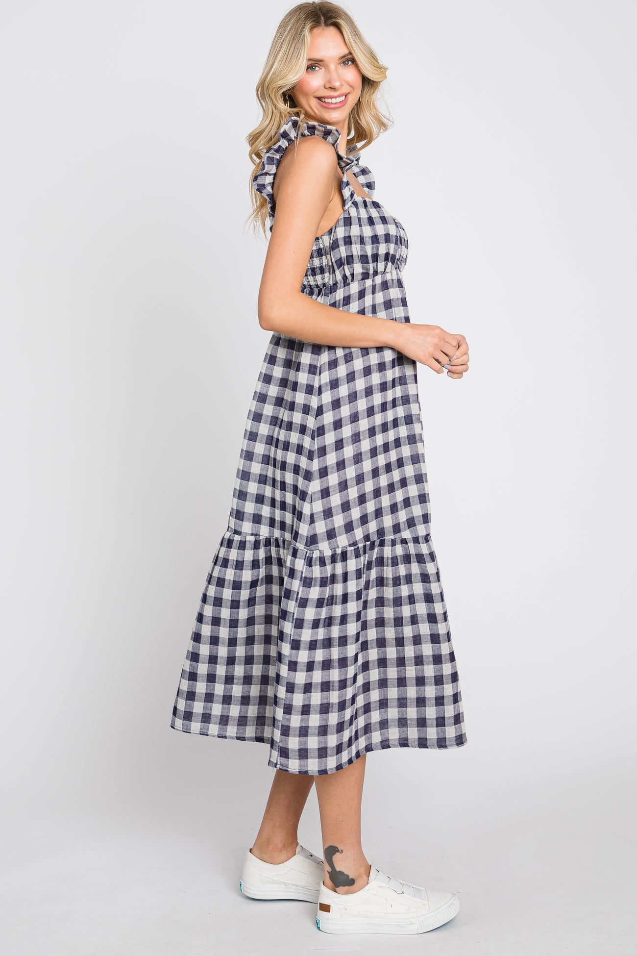 Woman wearing a navy and white gingham midi dress with ruffle straps and white sneakers
