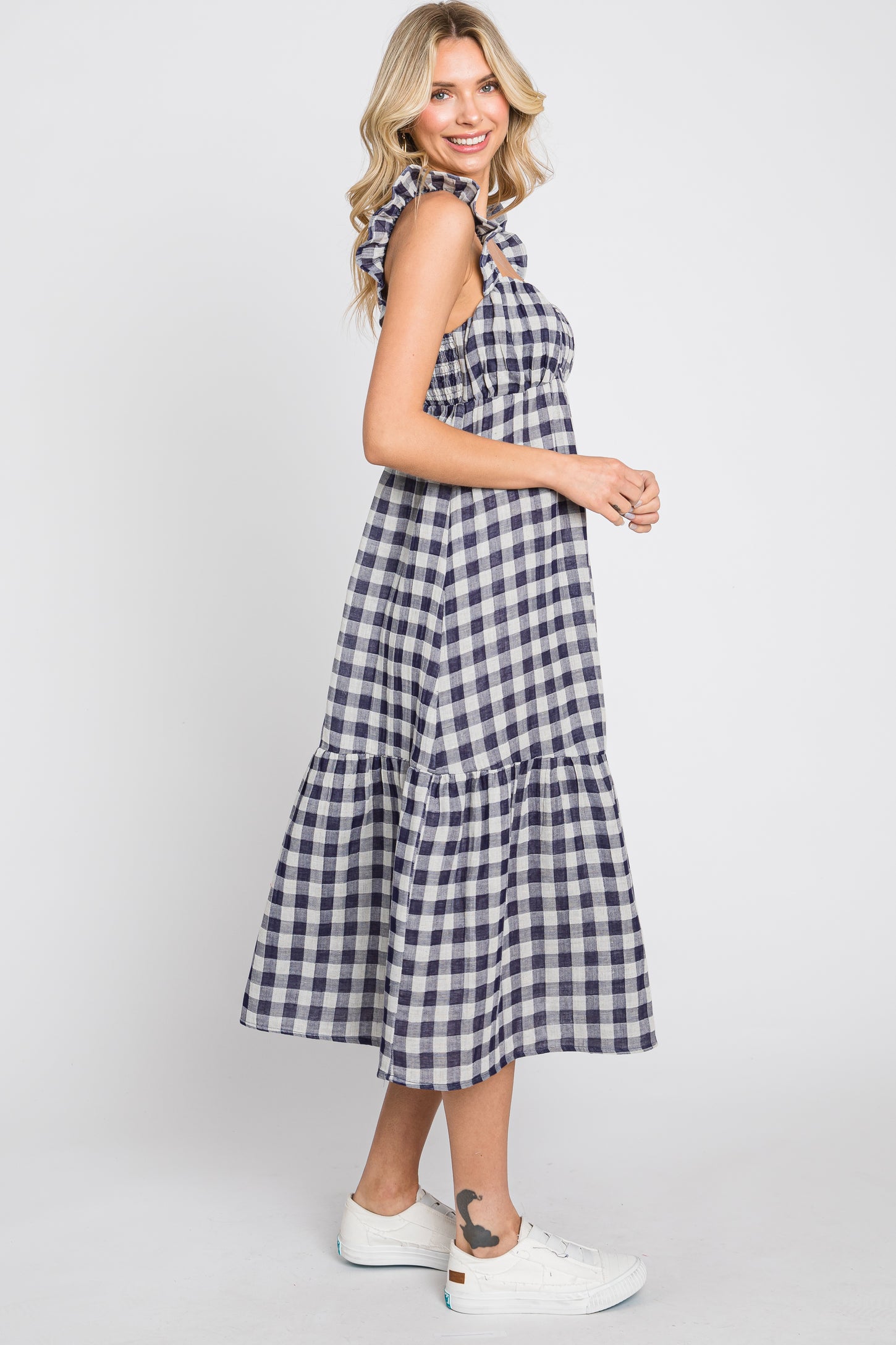 Woman wearing a navy and white gingham midi dress with ruffle straps and white sneakers