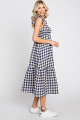 Woman wearing a navy and white gingham midi dress with ruffle straps and white sneakers