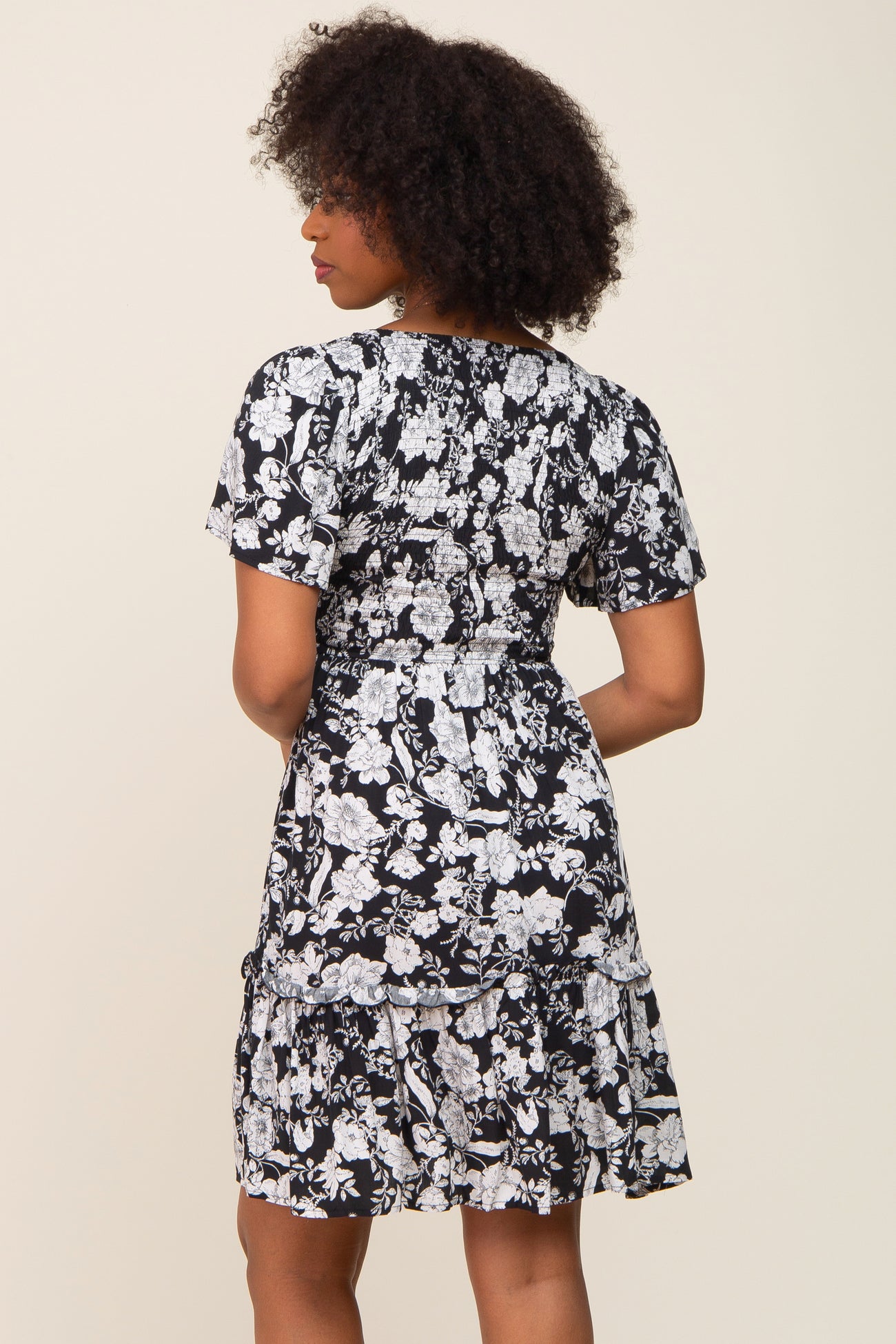 woman wearing a black and white floral short sleeve dress with a tiered skirt, viewed from the back