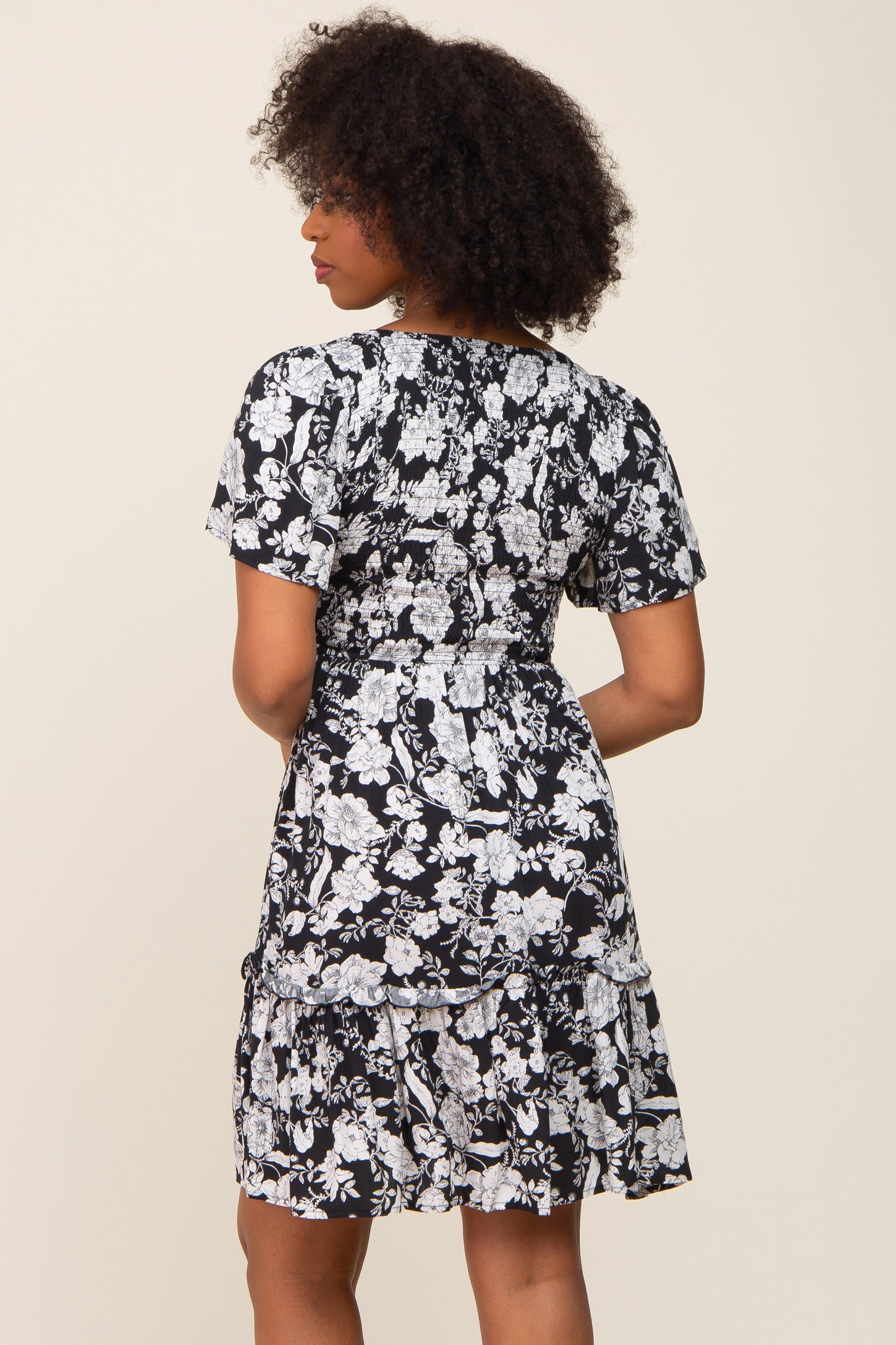 woman wearing a black and white floral short sleeve dress with a tiered skirt, viewed from the back