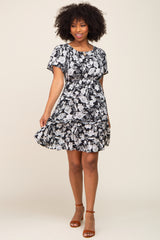 woman wearing a black floral print short sleeve dress with a tiered skirt and smiling.